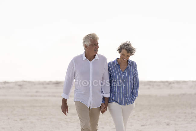 Felice coppia anziana che cammina sulla spiaggia tenendosi per mano — Foto stock