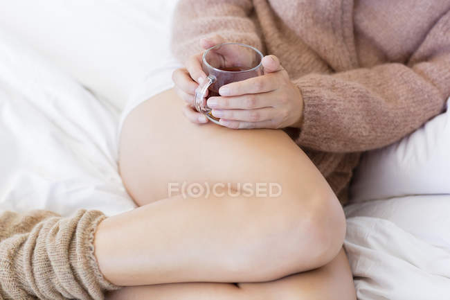 Крупный план женщины с чашкой травяного чая в постели — стоковое фото