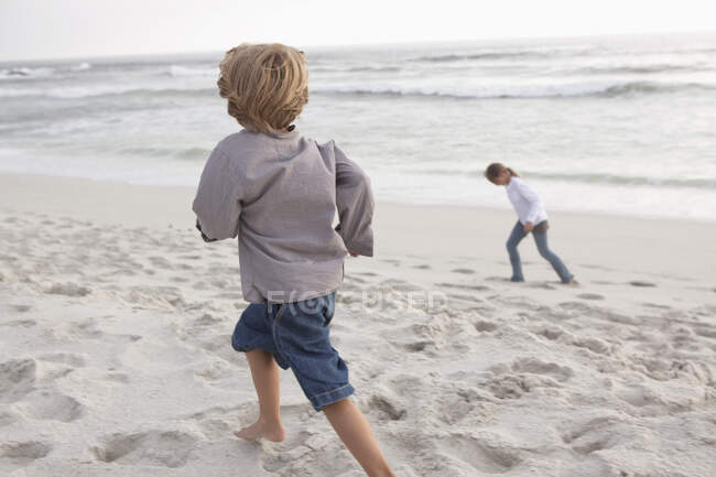 Visão traseira de um menino correndo na praia com sua irmã — Fotografia de Stock