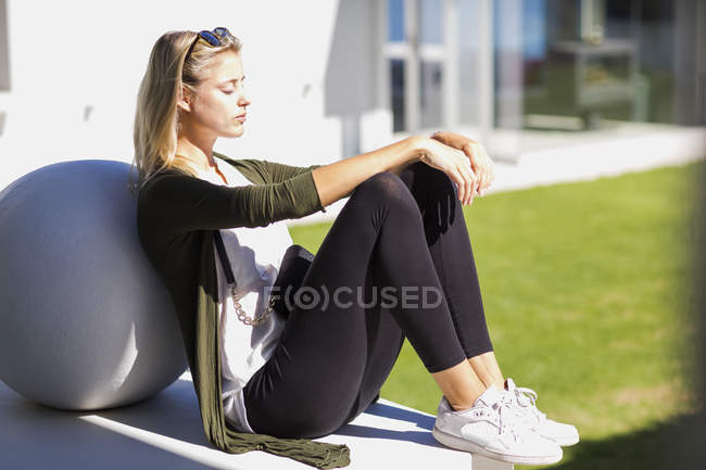 Молодая женщина расслабляется, опираясь на каменный шар на открытом воздухе — стоковое фото