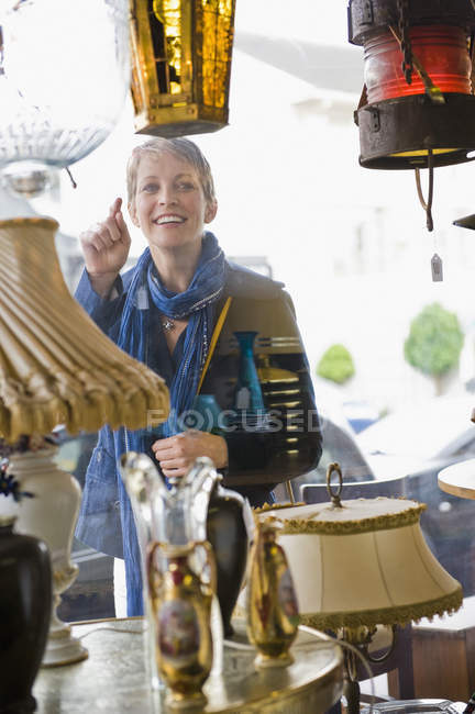 Femme souriante derrière la fenêtre regardant magasin — Photo de stock