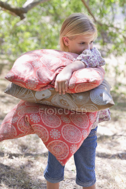 Retrato de una niña sonriente llevando almohadas al aire libre - foto de stock