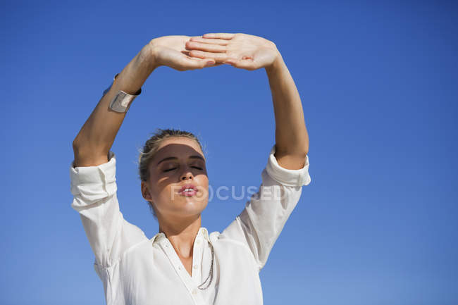 Jeune femme debout les yeux fermés contre le ciel bleu — Photo de stock