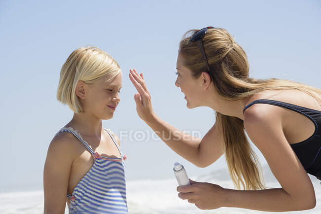 Belle femme appliquant de la crème solaire sur son visage de fille — Photo de stock