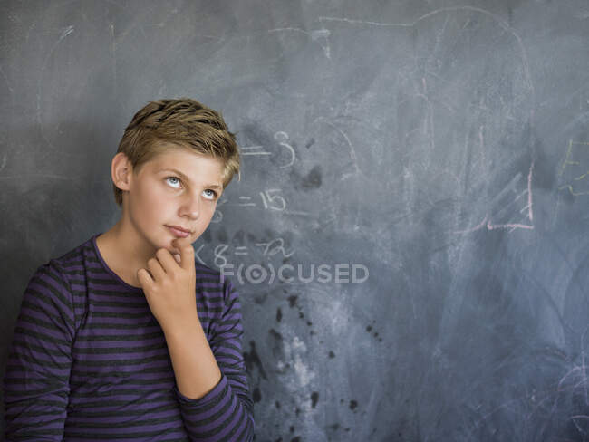 Niño pensando delante de una pizarra en un aula - foto de stock