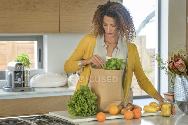 Mujer sacando comida de la bolsa de papel en la cocina - foto de stock