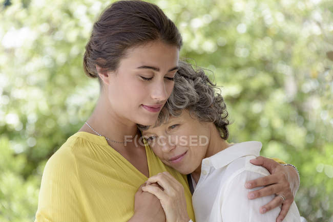 Retrato de una joven cariñosa abrazando a la madre al aire libre - foto de stock