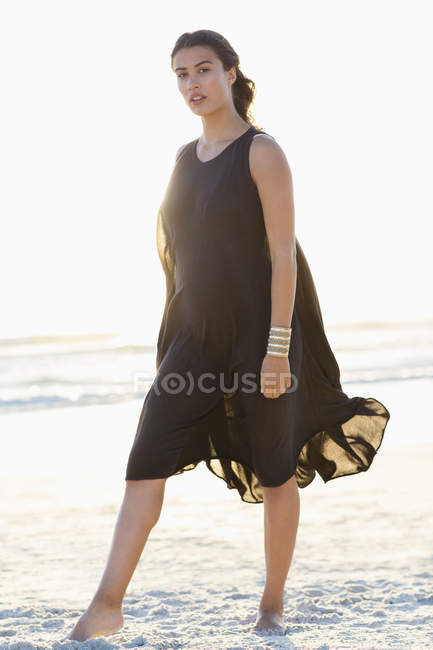 Porträt einer eleganten jungen Frau im schwarzen Kleid, die am Strand posiert — Stockfoto