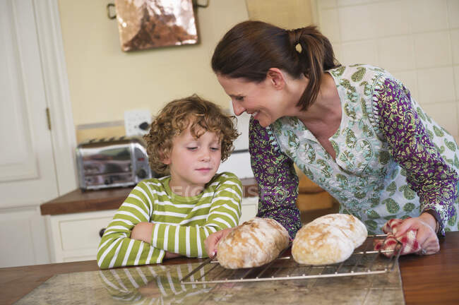 Cute little boy and mother baking bread in kitchen — Stock Photo