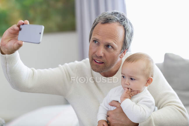 Счастливый отец с маленькой дочерью делает селфи с камерой телефона дома — стоковое фото