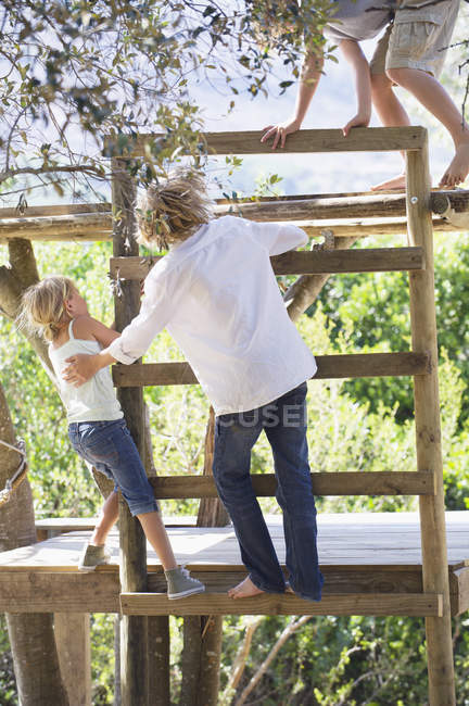 Children climbing ladders to tree house in garden — Stock Photo