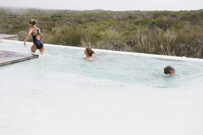 Zwei Mädchen schwimmen mit einem Jungen in einem Infinity-Pool — Stockfoto