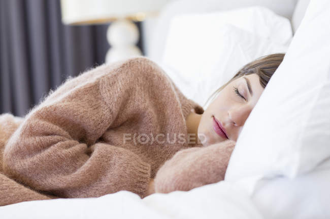 Young woman in comfy sweater sleeping on bed — Stock Photo