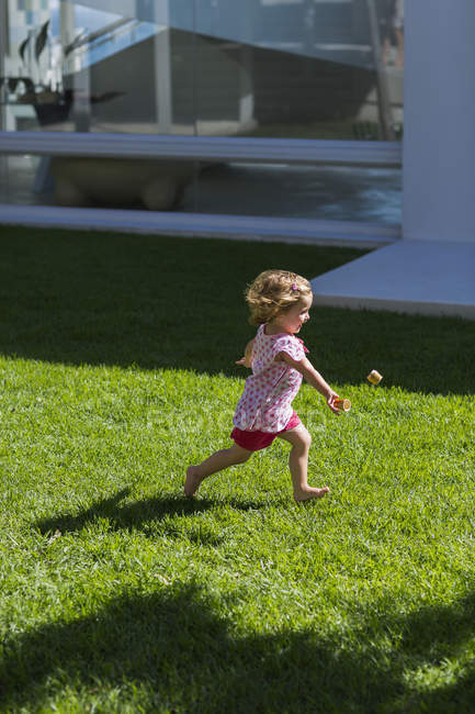Mignon bébé fille jouer sur l'herbe en face de la construction — Photo de stock