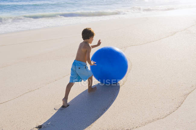 Маленький хлопчик грає з м'ячем на сонячному піщаному пляжі — стокове фото