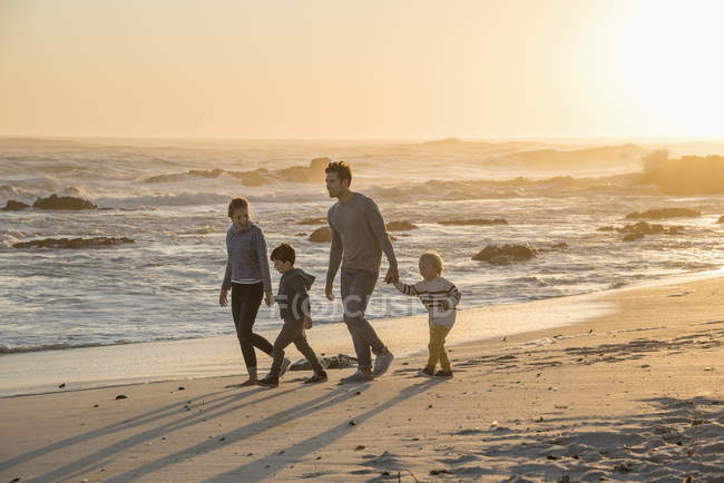 Familia feliz caminando en la playa de arena al atardecer - foto de stock