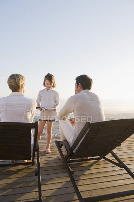 Girl reading book in front of parents on summer beach — Stock Photo