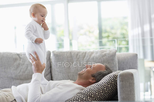 Père heureux couché sur le canapé et jouant avec la fille mignonne bébé à la maison — Photo de stock