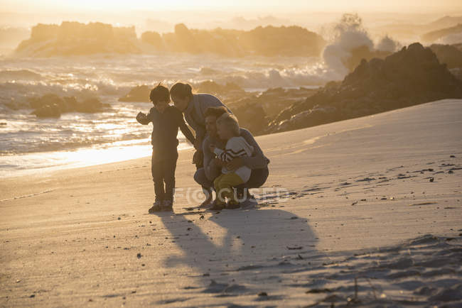 Família feliz se divertindo na praia ao pôr do sol — Fotografia de Stock