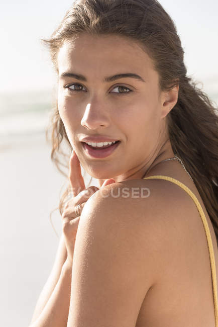 Retrato de mujer joven y bonita mirando por encima del hombro en la playa - foto de stock