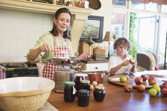 Abuela cocinando comida y niño pelando una manzana en casa - foto de stock