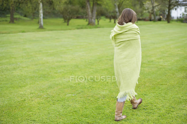 Chica envuelta en manta verde caminando en el campo - foto de stock