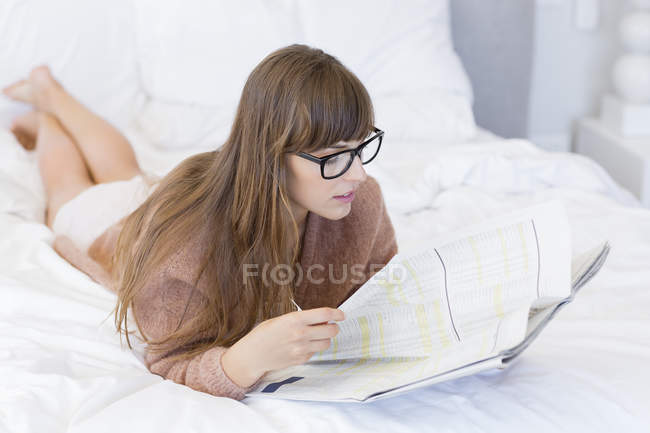 Junge Frau liest Zeitung auf dem Bett — Stockfoto