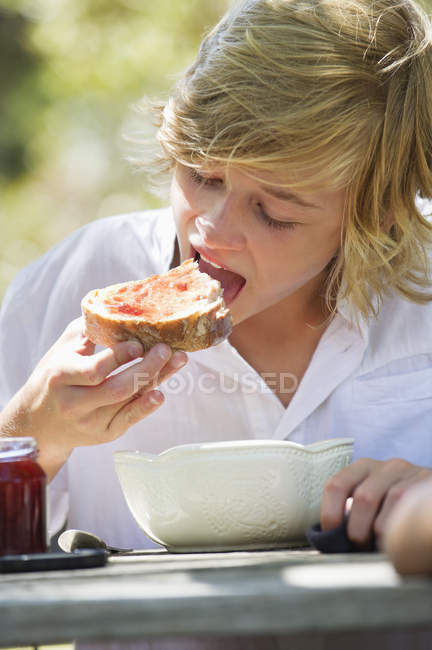 Retrato de un adolescente comiendo pan con mermelada al aire libre - foto de stock
