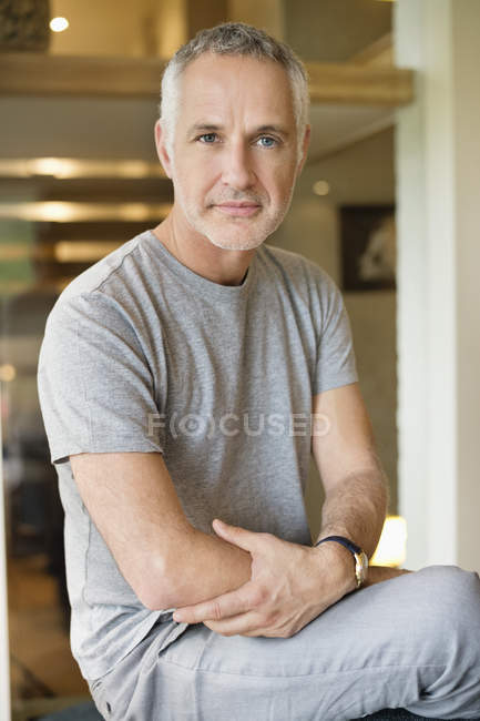Retrato de hombre maduro de pelo gris confiado sentado en casa - foto de stock