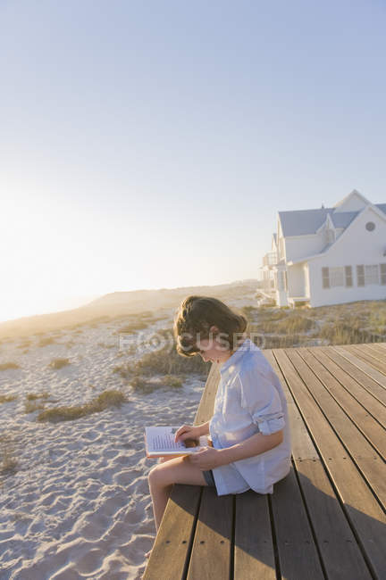 Маленькая девочка сидит на набережной на песчаном пляже и читает книгу — стоковое фото