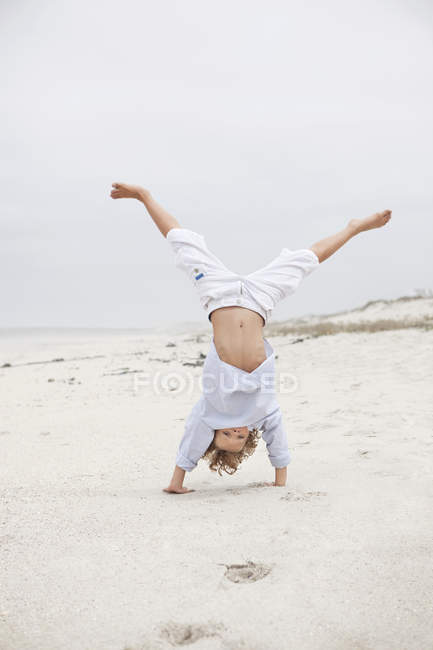 Fröhlicher Junge beim Handstand am Sandstrand — Stockfoto