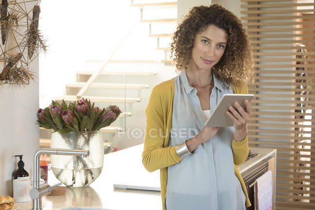 Вдумчивая женщина с помощью цифрового планшета на кухне — стоковое фото