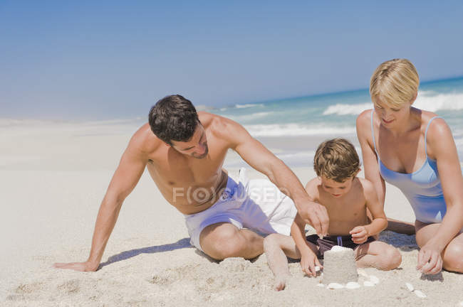 Familia haciendo castillo de arena en la playa - foto de stock