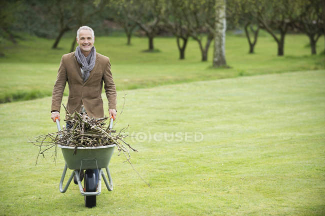 Eleganter älterer Mann sammelt Brennholz auf der grünen Wiese — Stockfoto
