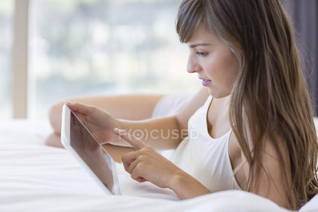 Молода жінка лежить на ліжку і використовує цифровий планшет — стокове фото