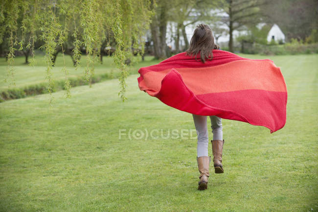 Girl wrapped in red blanket walking in field — Stock Photo