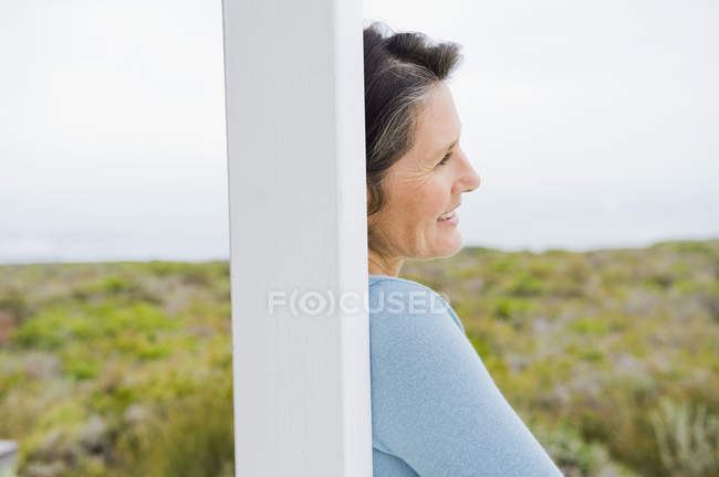 Nahaufnahme einer lächelnden Frau, die tagträumt, während sie sich in der Natur an einen Pfosten lehnt — Stockfoto