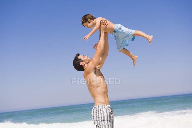 Человек играет с сыном на пляже под голубым небом — стоковое фото