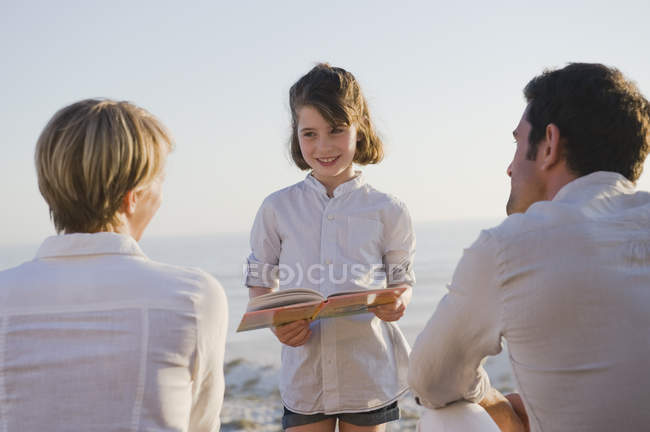 Mädchen liest Buch vor Eltern am Strand — Stockfoto