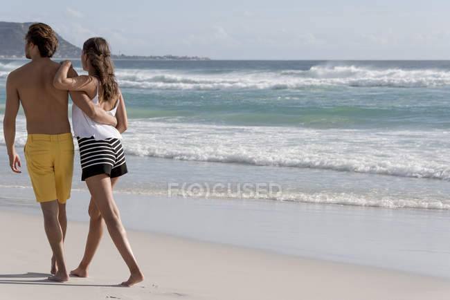 Rear view of young romantic couple walking on sandy beach — Stock Photo
