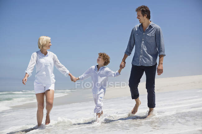 Pareja caminando en la playa con su hijo - foto de stock