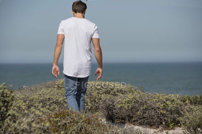 Visão traseira do jovem caminhando na costa do mar — Fotografia de Stock