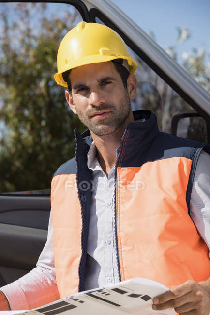 Retrato del ingeniero masculino sosteniendo el plano en la furgoneta - foto de stock