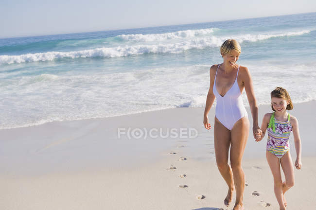 Mujer caminando en la playa de arena con su hija - foto de stock