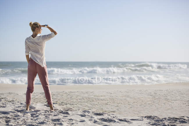 Grande jeune femme debout sur la plage ensoleillée — Photo de stock