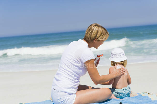 Mulher aplicando loção bronzeado do sol em sua filha na praia — Fotografia de Stock