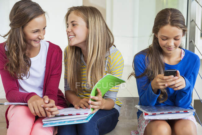 Alumnas sentadas en el escalón de la escuela y hablando - foto de stock
