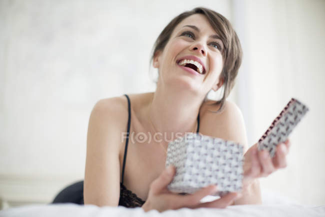 Елегантна щаслива жінка тримає подарункову коробку, лежачи на ліжку — стокове фото