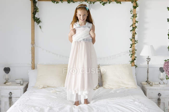 Portrait of a girl standing on bed and trying dress — Stock Photo