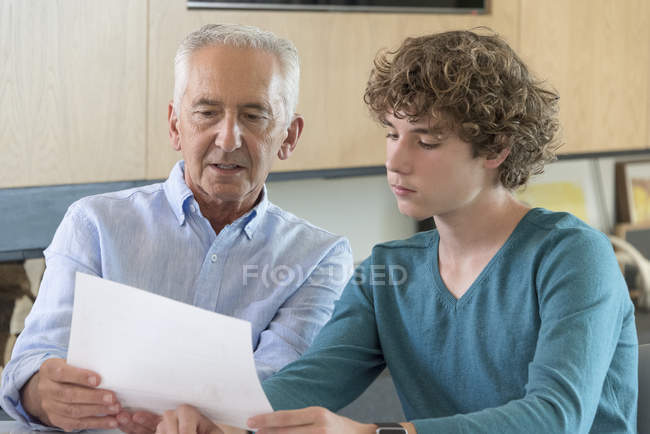 Hombre mayor haciendo papeleo con su nieto en el salón - foto de stock